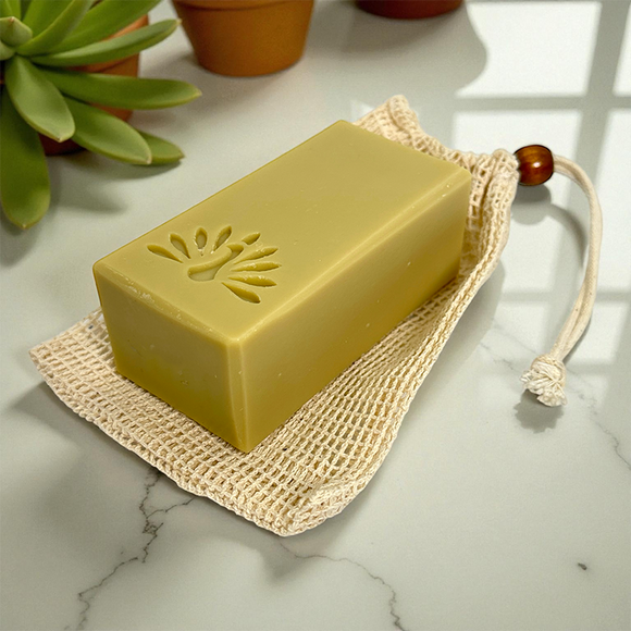 Yellow bar of soap on a natural fiber soap bag with plants in the background