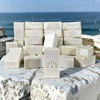 Stack of olive oil soap bars on a stone surface by the ocean.