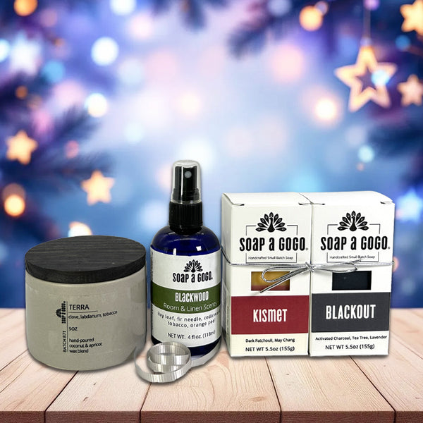 Collection of personal care products including a candle, room spray bottle, and 2 boxed soaps on a wooden surface with a festive background.