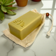 Yellow bar of soap on a natural fiber soap bag with plants in the background