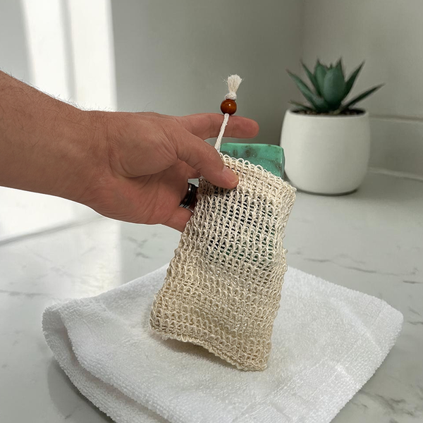 Hand holding a textured soap bag with a plant in the background