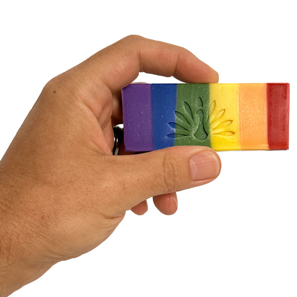 Hand holding a rainbow-colored soap with embossed logo on a white background