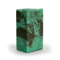 Side view of green and gray swirled soap bar with with peacock logo on a white background