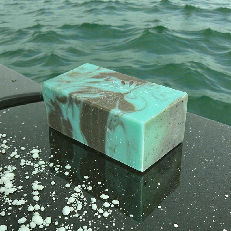 Marble-patterned bar of soap on a wet stone slab surface with ocean water in the background