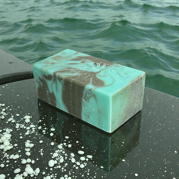 Marble-patterned bar of soap on a wet stone slab surface with ocean water in the background