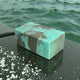 Marble-patterned bar of soap on a wet stone slab surface with ocean water in the background