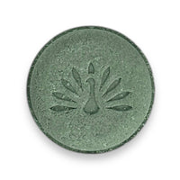 A round green shampoo bar with a peacock logo pattern on the top surface.