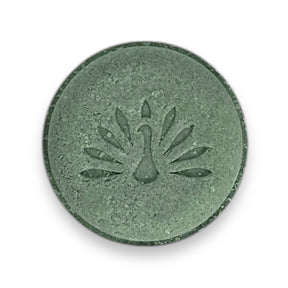 A round green shampoo bar with a peacock logo pattern on the top surface.
