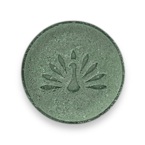 A round green shampoo bar with a peacock logo pattern on the top surface.