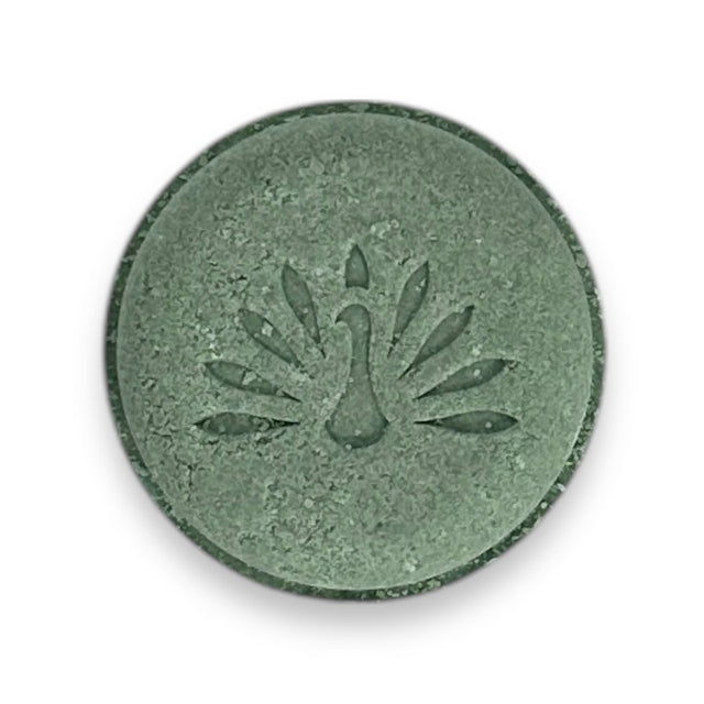 A round green shampoo bar with a peacock logo pattern on the top surface.