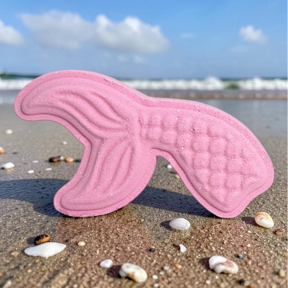 Pink mermaid tail bath bomb on a sandy beach with ocean waves in the background