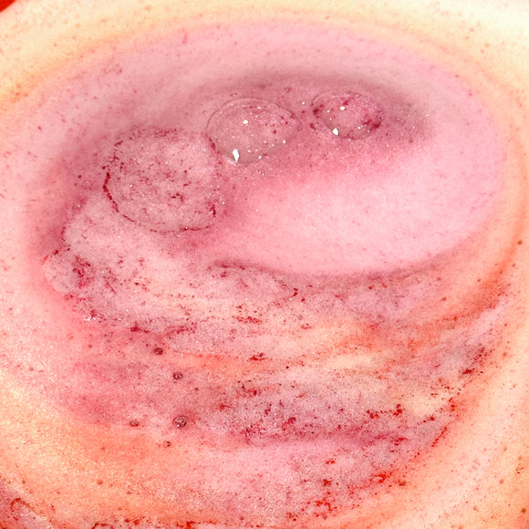 Sundance Swirl bath bomb activated in water. Bands of color and foam in shades of pink, red, orange, and yellow