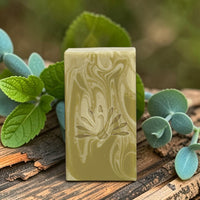 Natural bar soap on a cedarwood surface surrounded by botanicals