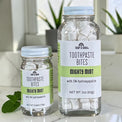 Two clear glass jars of Soap A GoGo Toothpaste Bites in Mighty Mint flavor, one small and one large, with white toothpaste bites visible inside and mint leaves on a light marble surface.